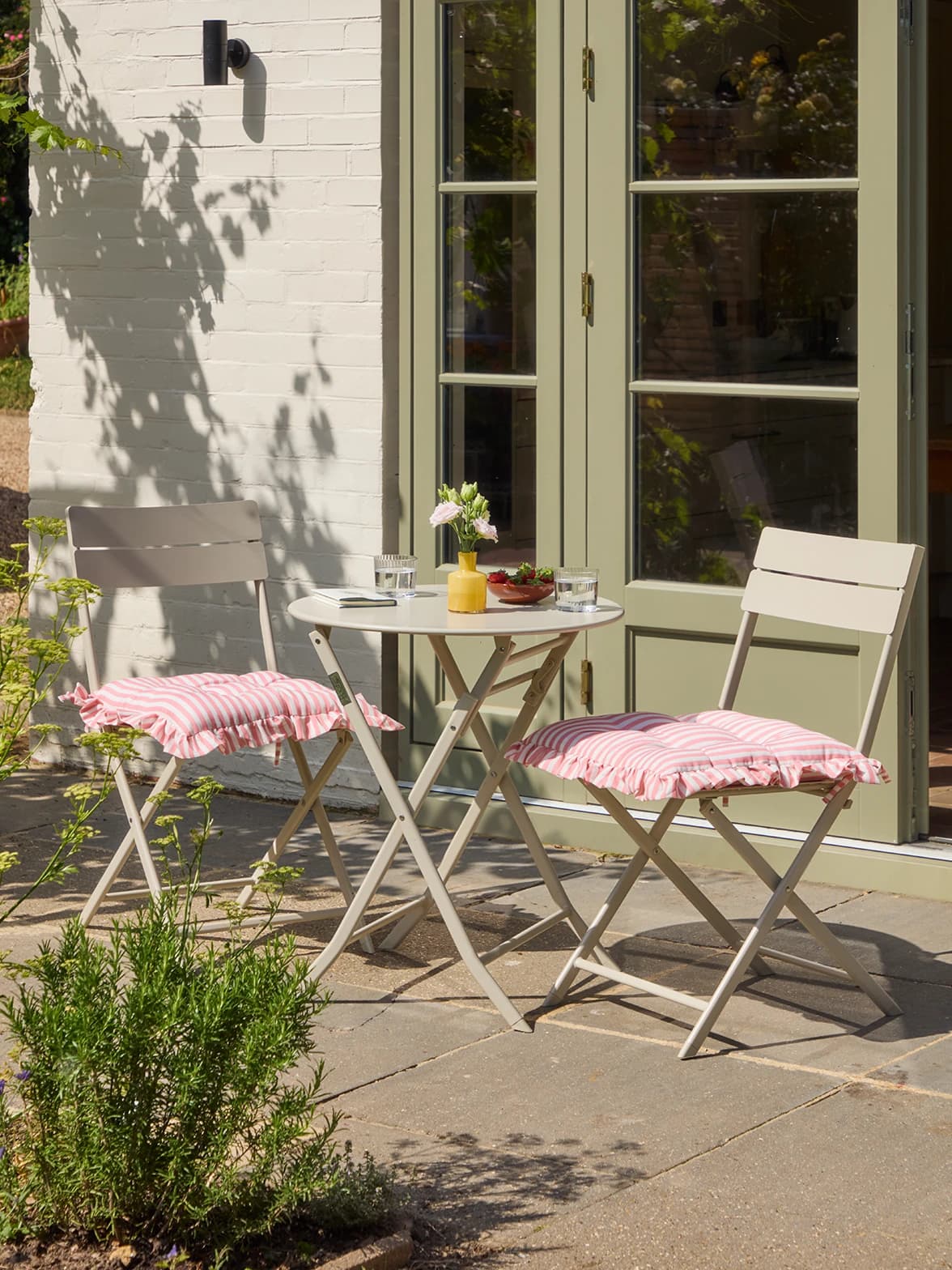 A bistro table and chairs with stripe cushions on sunlit patio