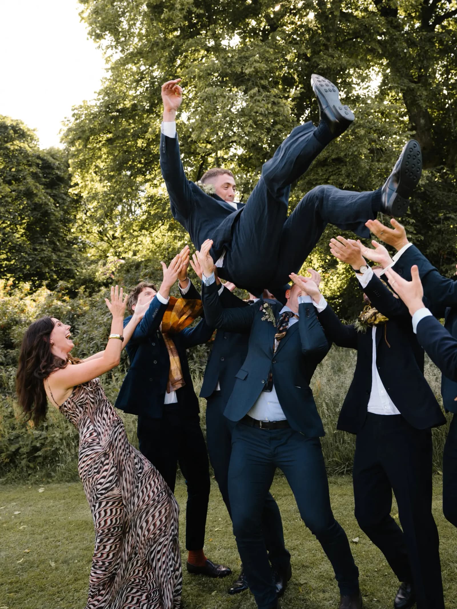 Groomsmen throwing the groom into the air as a guest cheers on the lawn at a Studio 54 themed festival wedding in Scotland