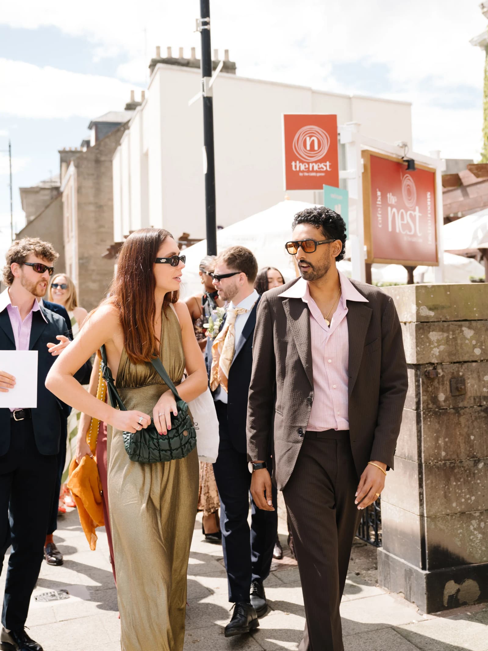 Stylish guests in Seventies-inspired suits and a silk jumpsuit walking to the church in Forfar for a festival wedding in Scotland