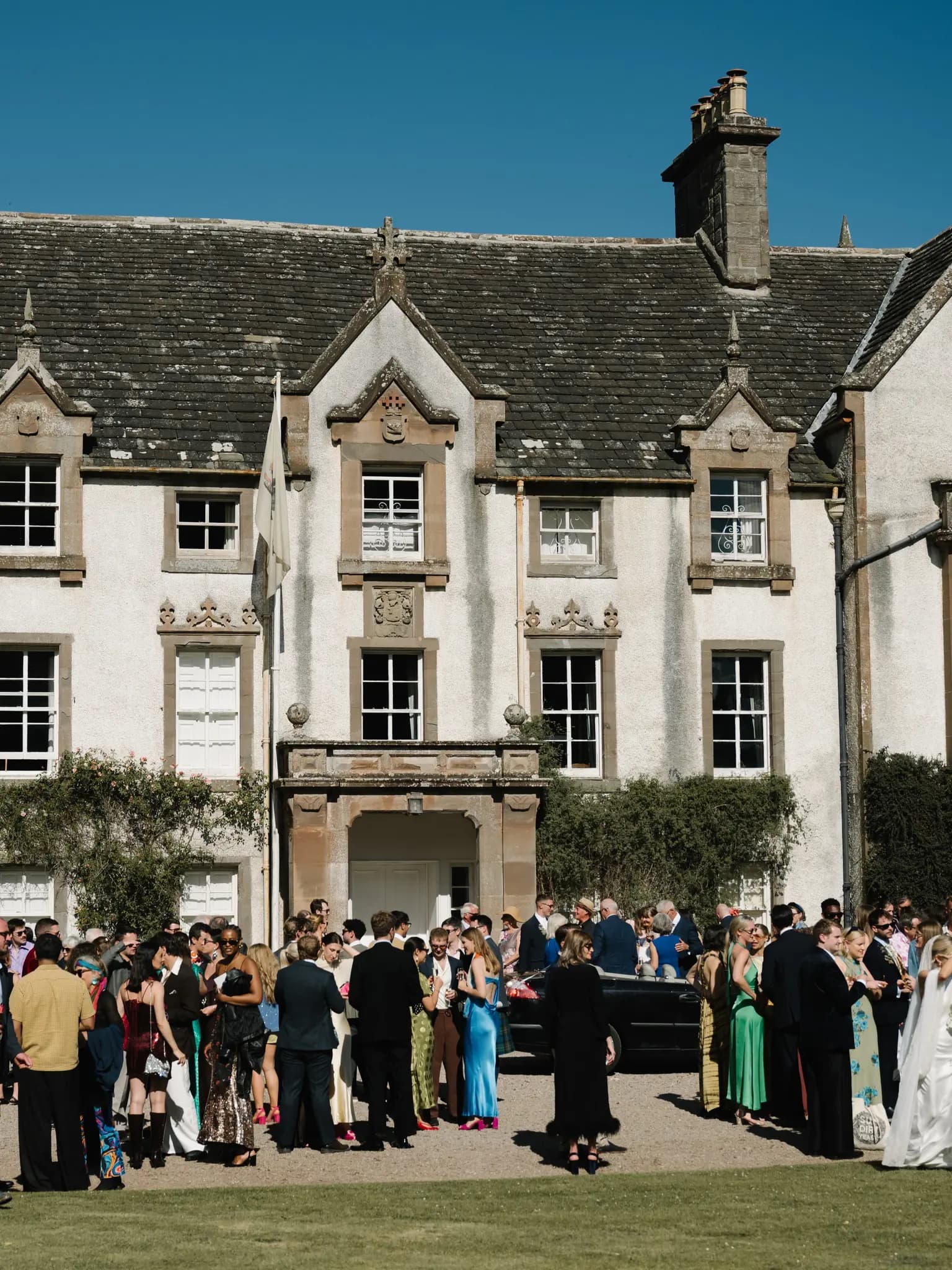 Wedding guests in colourful Studio 54 outfits gathered for drinks on the lawn in front of Middleton House in Scotland